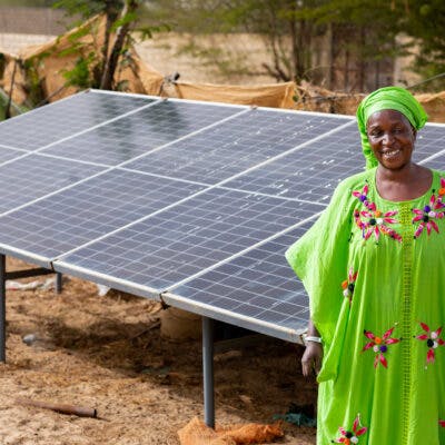 African woman in traditional wear in front of solar panel