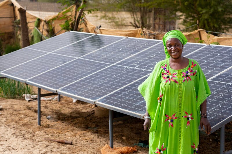 African woman in traditional wear in front of solar panel