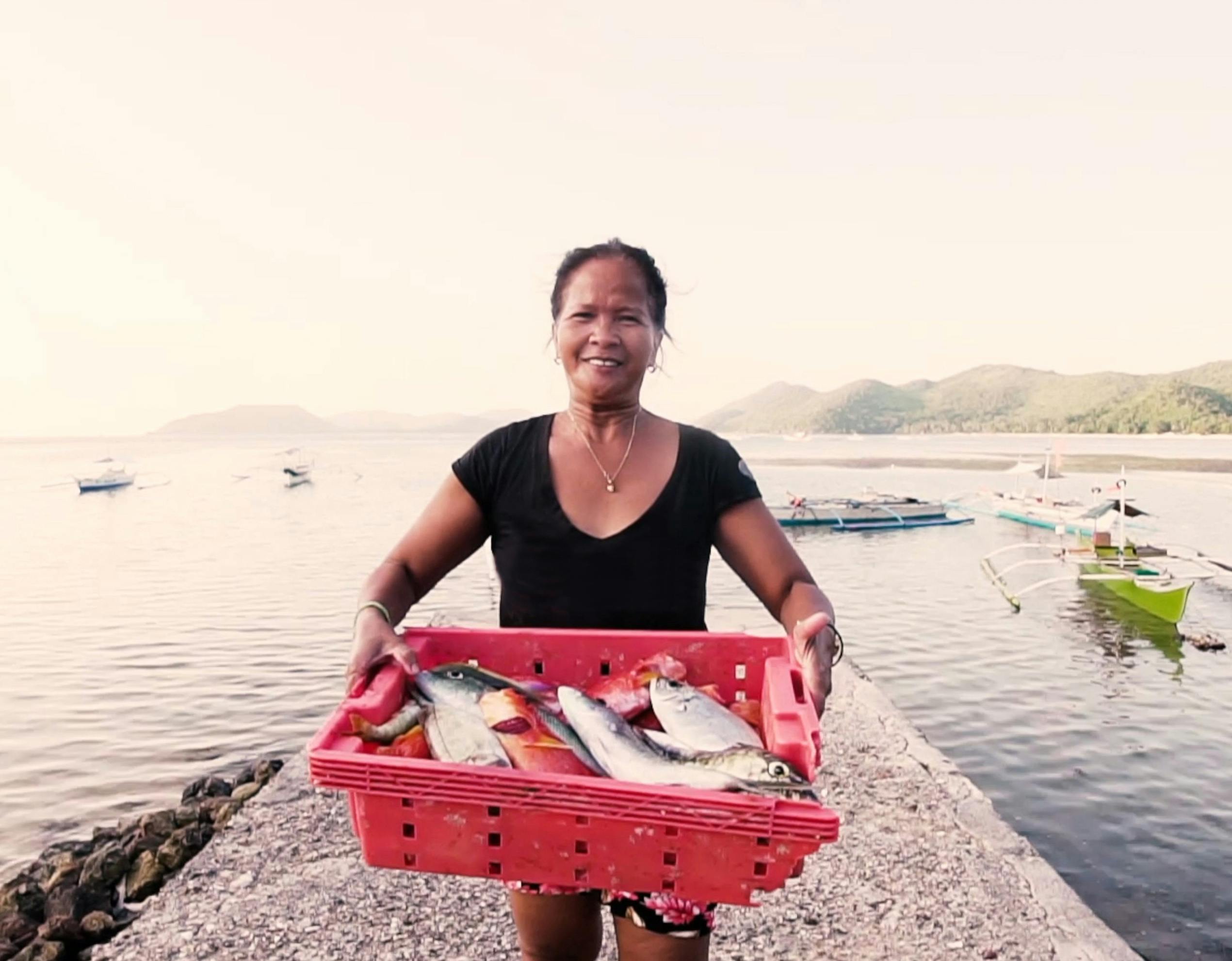 Woman holding a crate of fish by the river